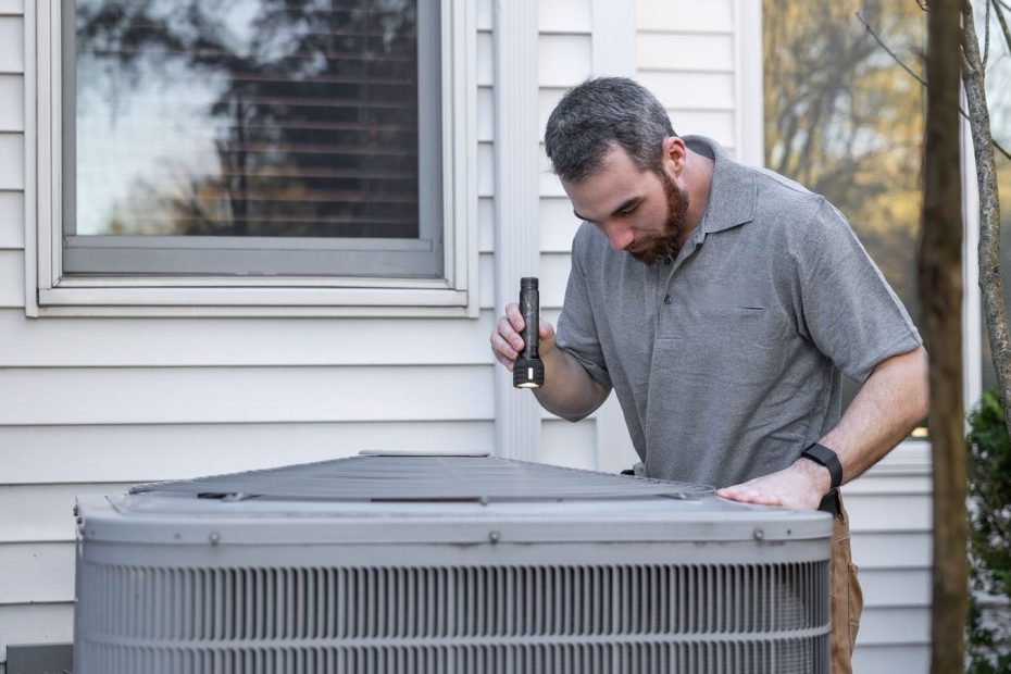 Technician with a flashlight inspecting an outdoor AC condenser, the work an HVAC marketing agency promotes