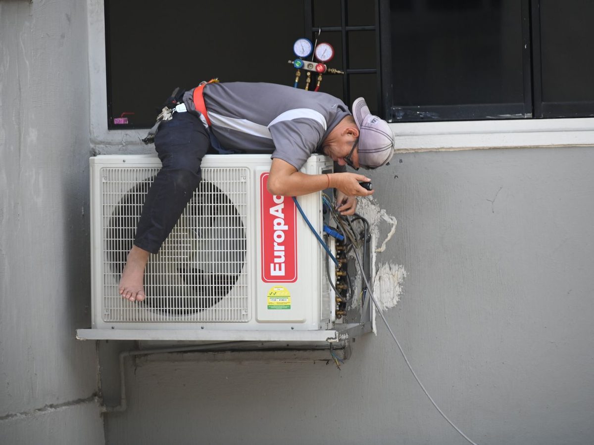Technician repairing a wall-mounted outdoor air conditioning unit