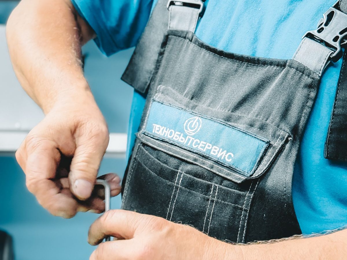Plumber in a blue uniform repairing a pipe inside a home