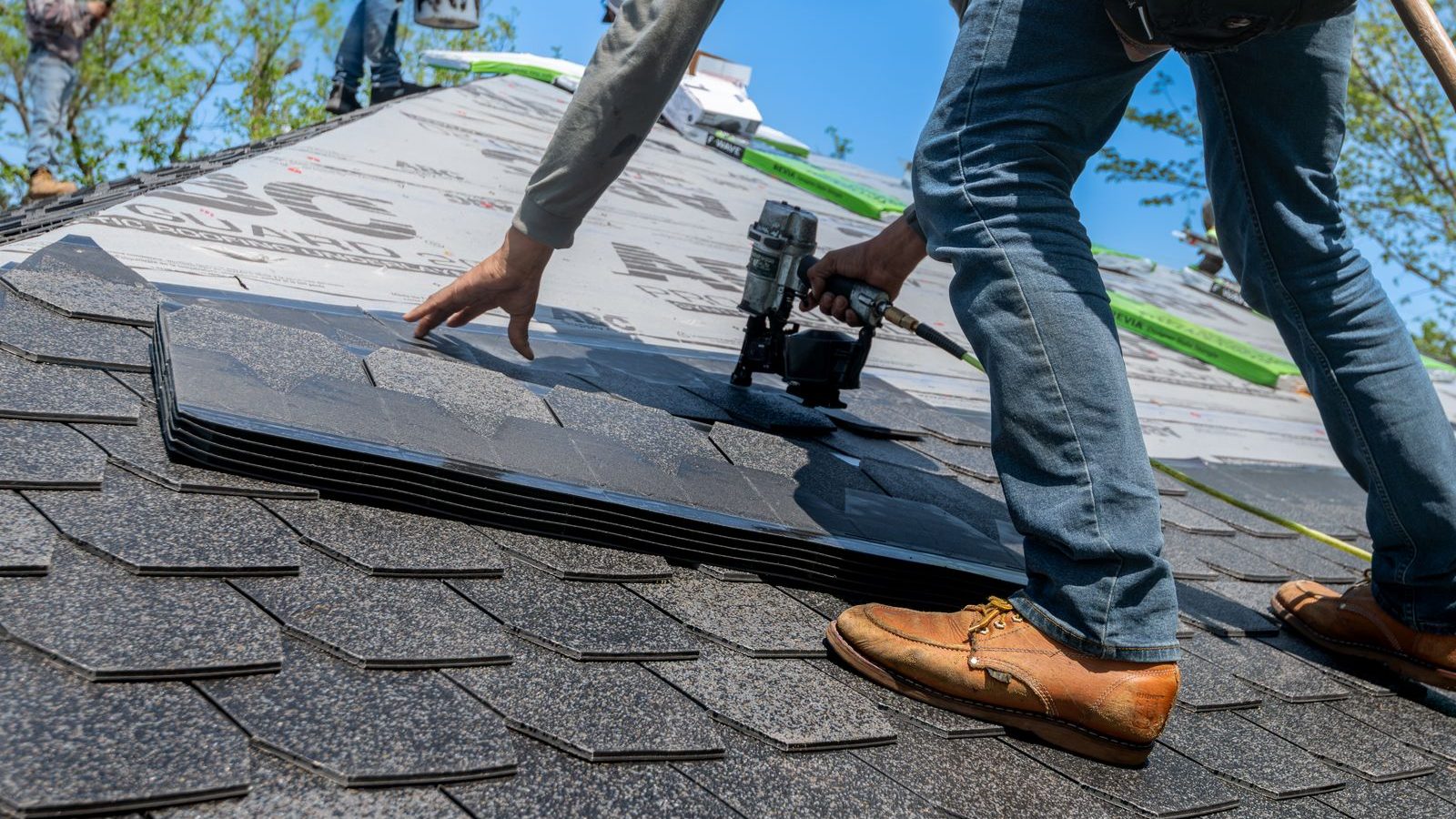 Roofing SEO: roofer kneeling on a pitched roof installing asphalt shingles