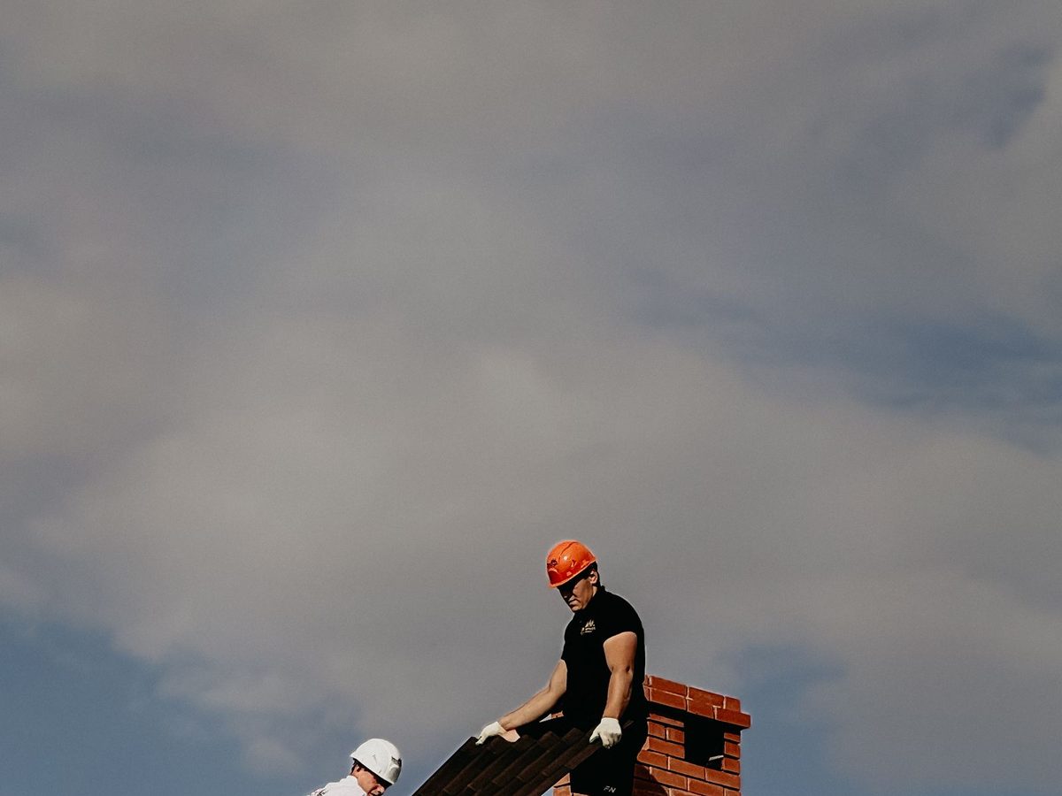 Two roofers repairing a roof under a cloudy sky